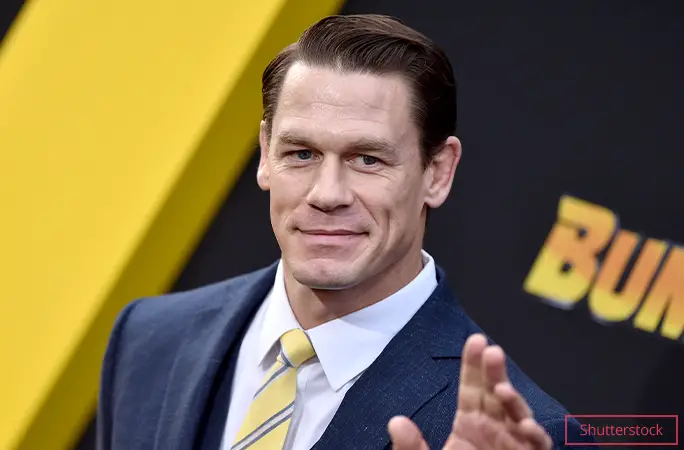 John Cena in suit and yellow tie waving at camera