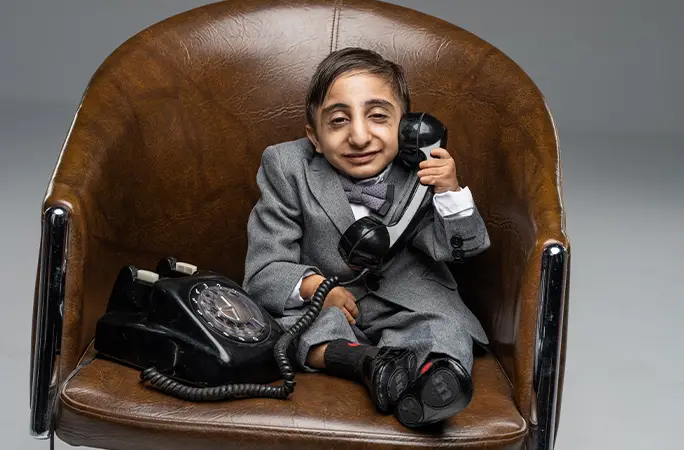 World shortest man sitting on a chair holding a phone