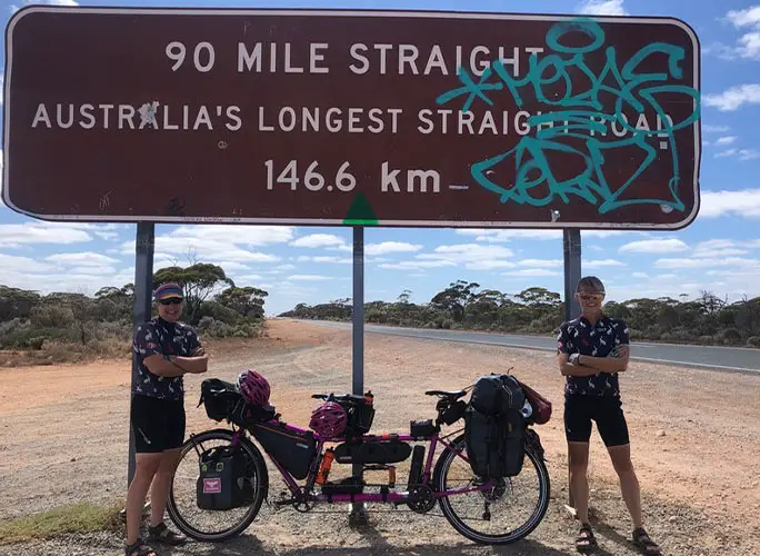 cat and raz posing in front of sign for the longest straight road in Australia