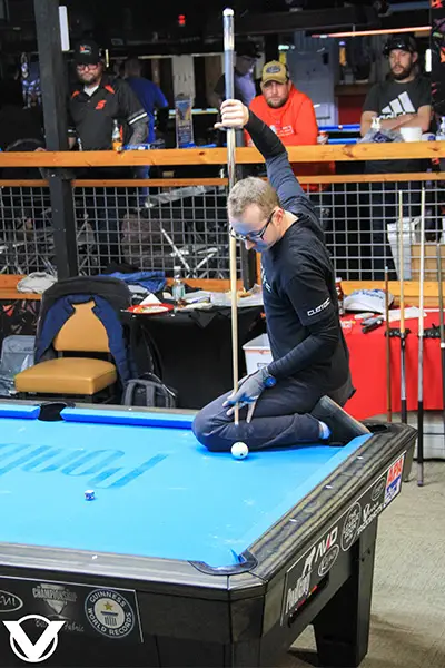 florian kohler lining up a shot with one leg on the table