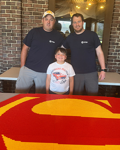 Bryce Matt and Greg standing next to LEGO symbol