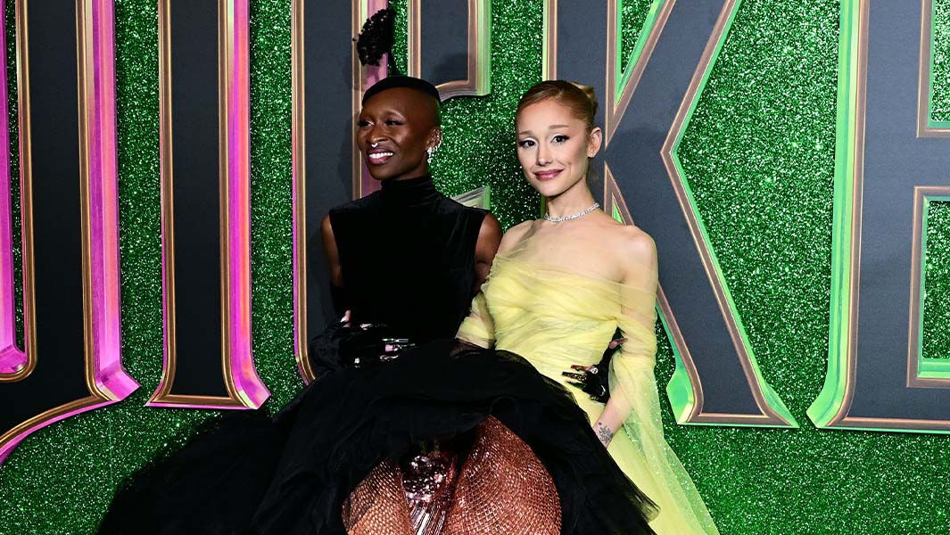 Ariana Grande and Cynthia Erivo stood in front of a giant Wicked logo on a red carpet