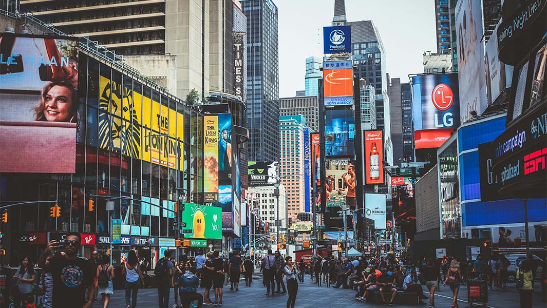 A view of a street in Broadway with signs for theatre shows and lots of people gathered