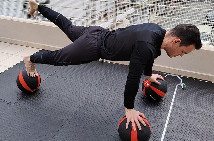 George doing push ups on medicine balls with one leg raised
