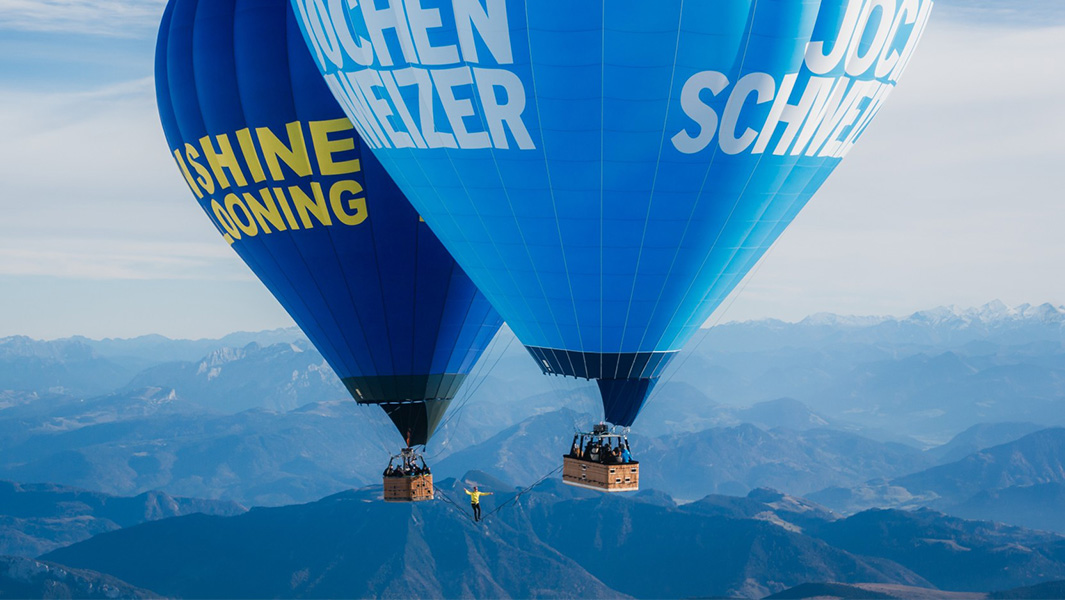 Man walking across slackline suspended between two hot air balloons