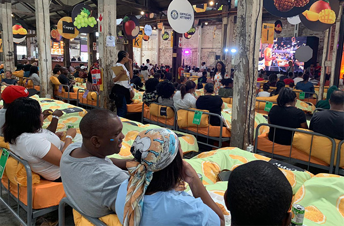 A crowd of people in beds in a large room, eating breakfast
