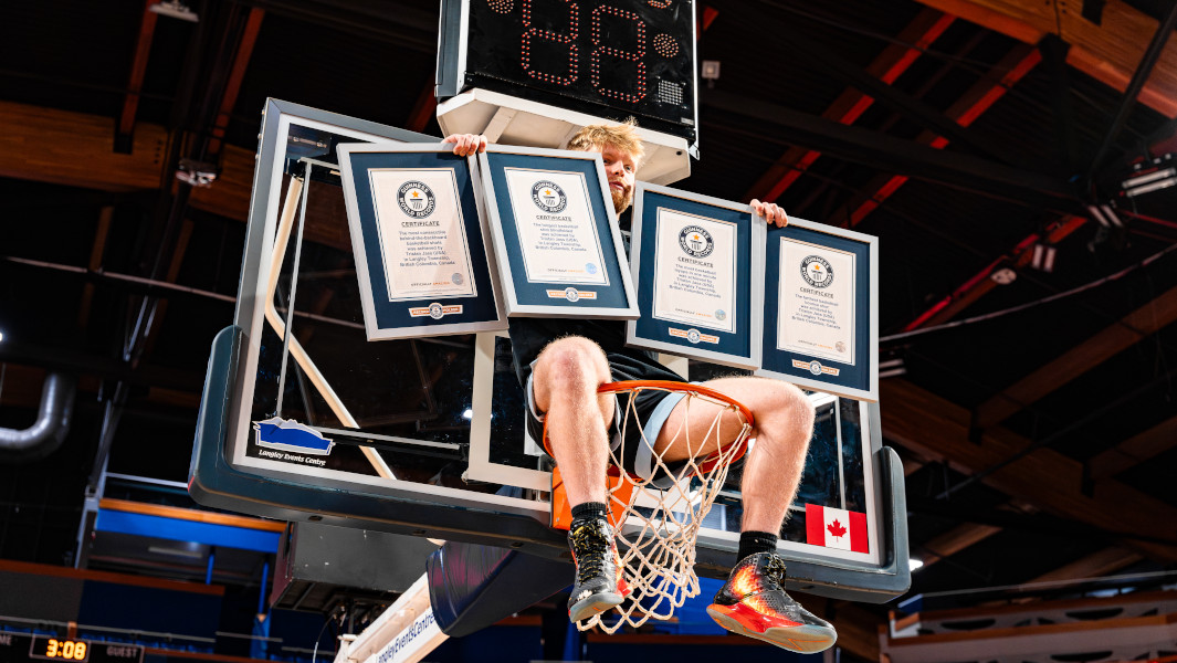 Tristan Jass sitting on the rim of a basketball net holding four GWR certificates