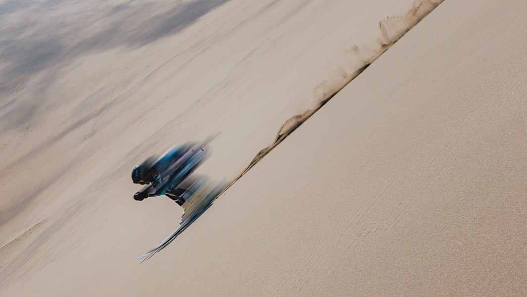 Split image of Mahe holding his skis and going downhill on the sand dune