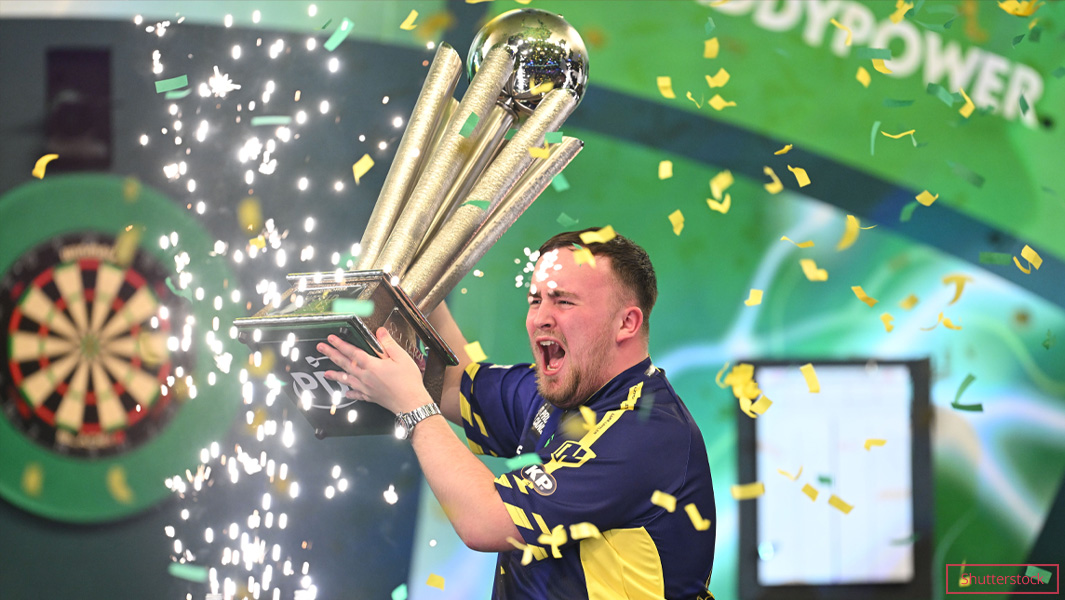 Luke Littler holding a trophy on a stage
