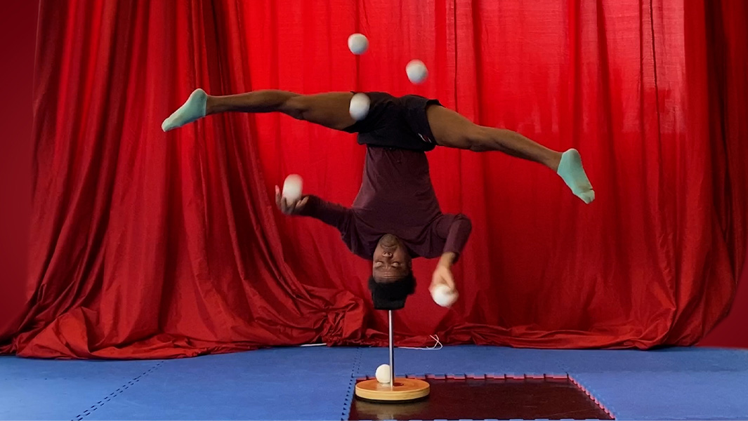 Jose juggling while balacing on his head