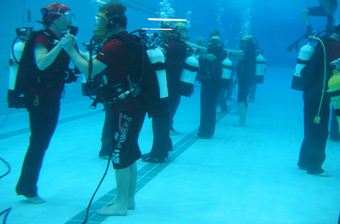 Couples lined up dancing underwater in scuba gear