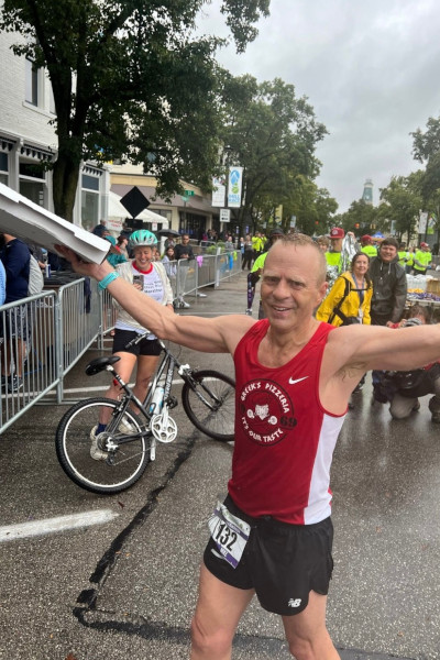 Mike Cole smiling holding his pizza box running past the finish line