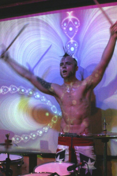 Col shirtless and playing the drums