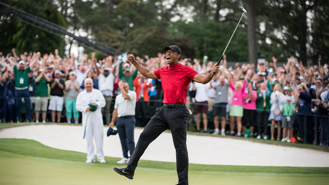 Tiger Woods in a red golf shirt with his arms out celebrating