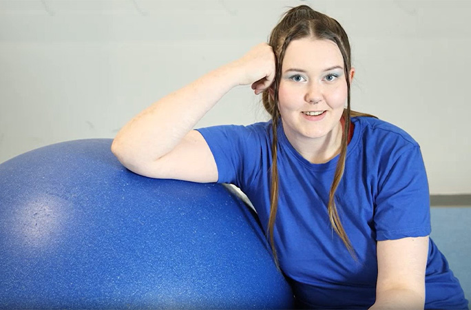 Jasmin talking to the camera and resting her elbow on a rolling globe