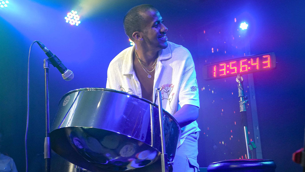Joshua playing the steelpan on stage with a clock behind him
