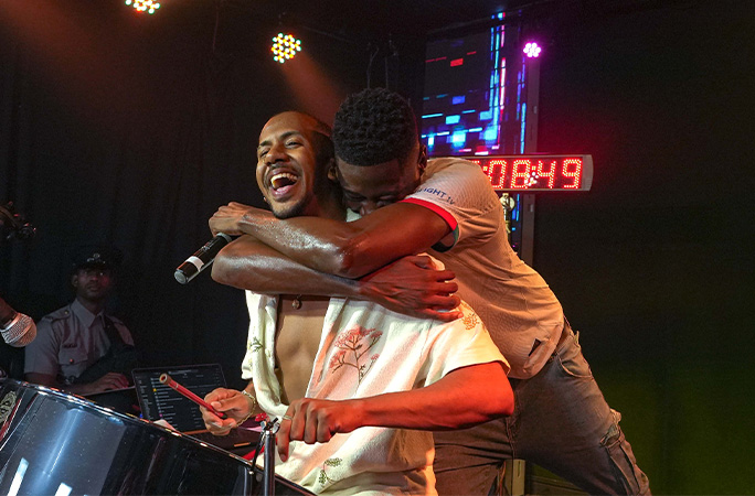 Joshua being hugged as he plays steelpan