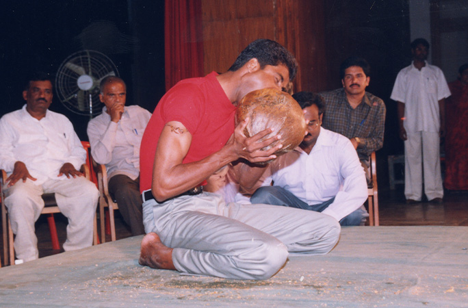 man husking a coconut with his teeth