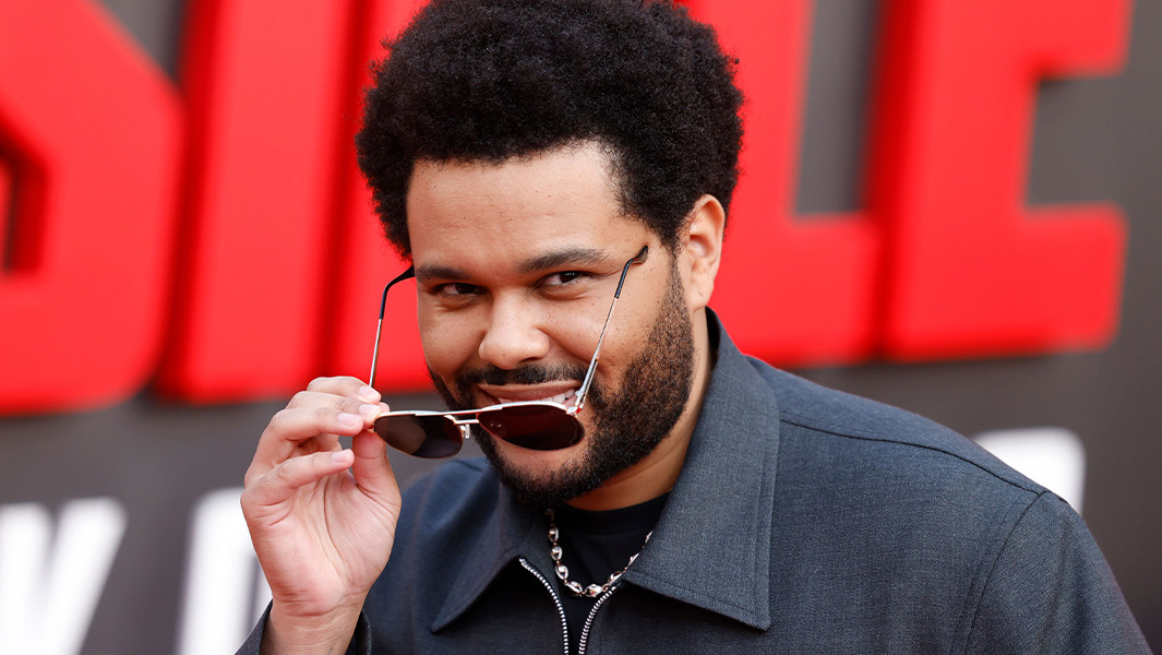 The Weeknd on a red carpet pulling his sunglasses down to look at the camera
