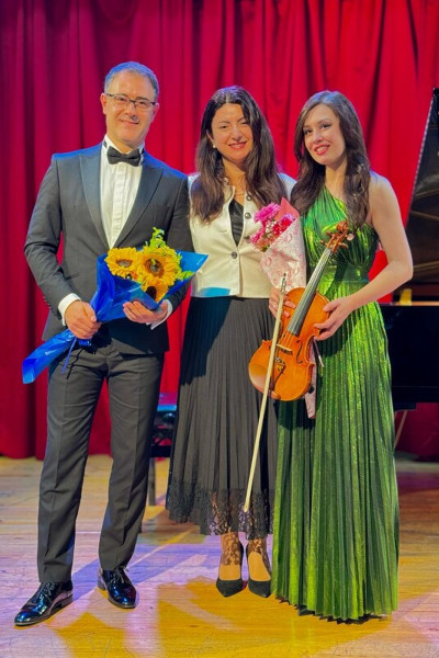Diana and Stefan onstage holding flowers and taking a photo with a presenter