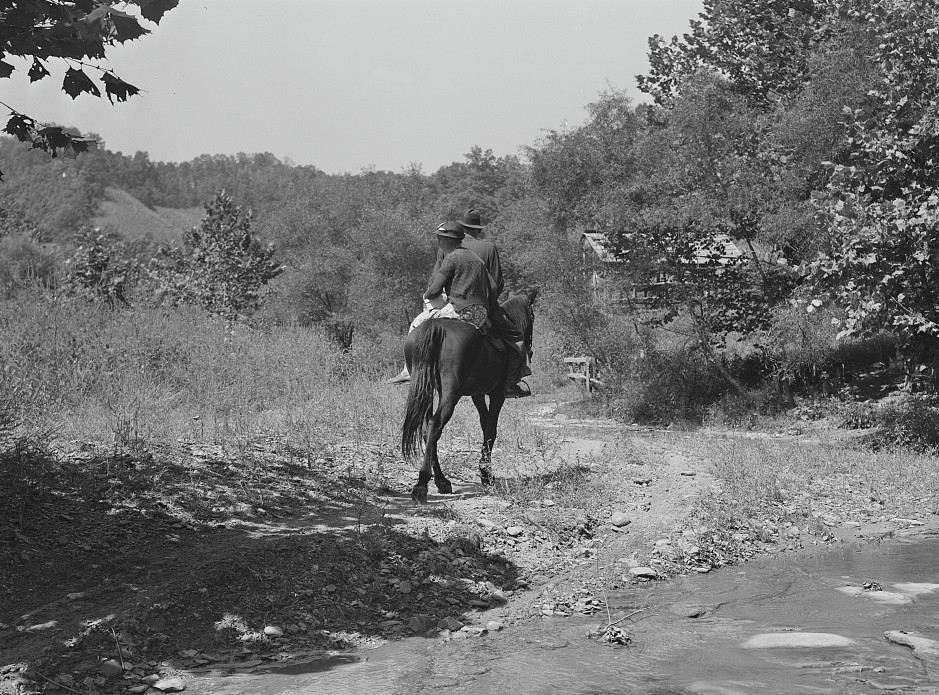 A couple on horseback crossing a stream