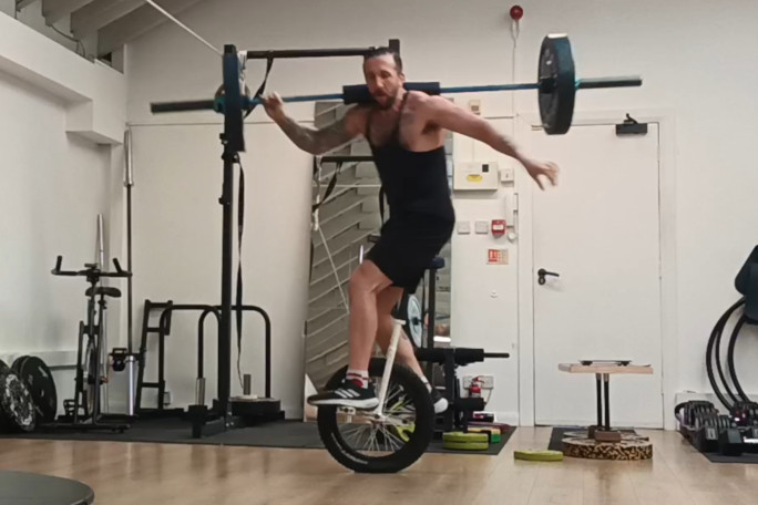 Jason midattempt, holding the barbell with one hand, and standing on the unicycle