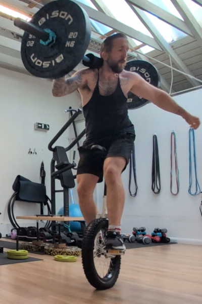 Jason holding the weight with one arm, while riding his unicycle
