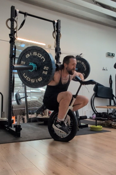 Jason, midsquat, on the unicycle holding the weight