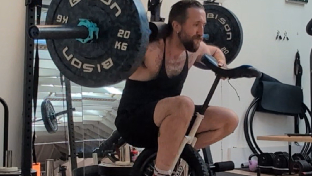 Split image of two different angles of Jason completing the squat with the barbell and unicycle
