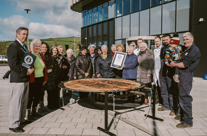 a group of people gathered around the largest Welsh cake