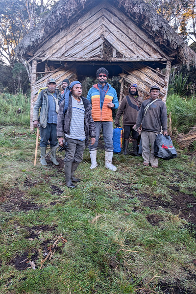 Anmish with other people in front of wooden hut