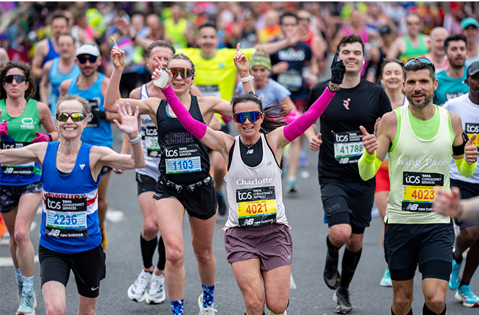a woman in brown running gear cheers while running the london marathon