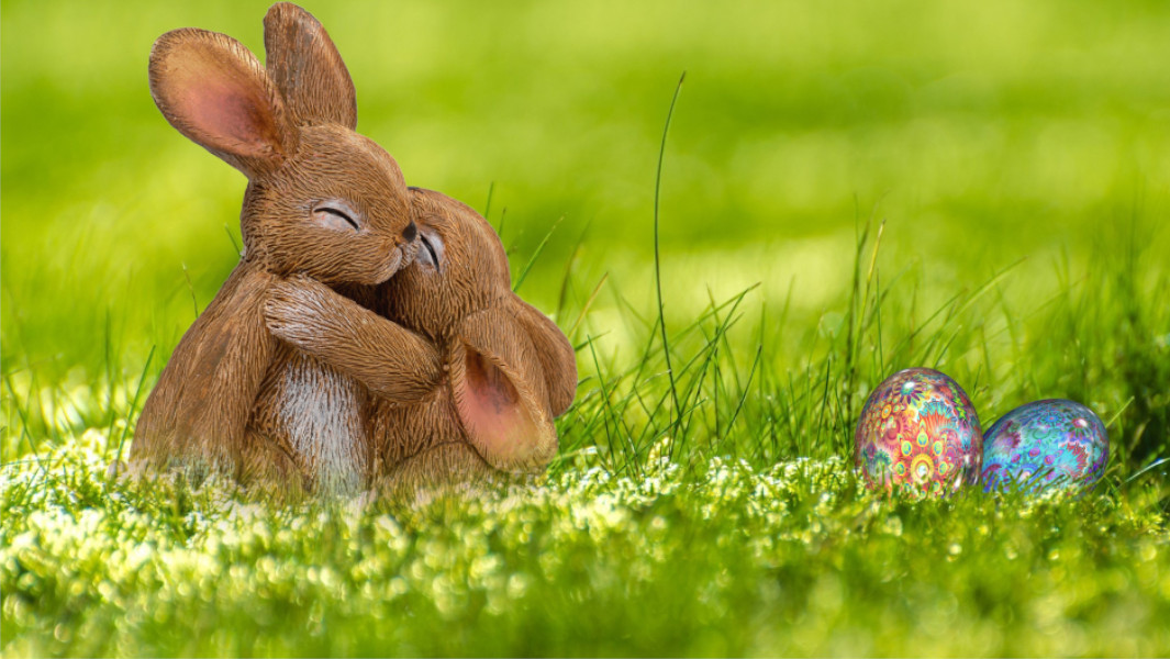 Two bunnies hugging in a meadow next to Easter eggs