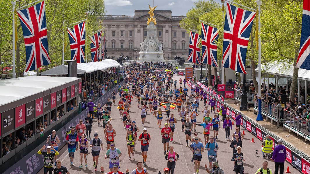 a crowd runs in the london marathon with buckingham palace in the background