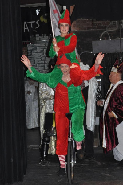 Linda and a child dressed in red and green unicycling across the stage