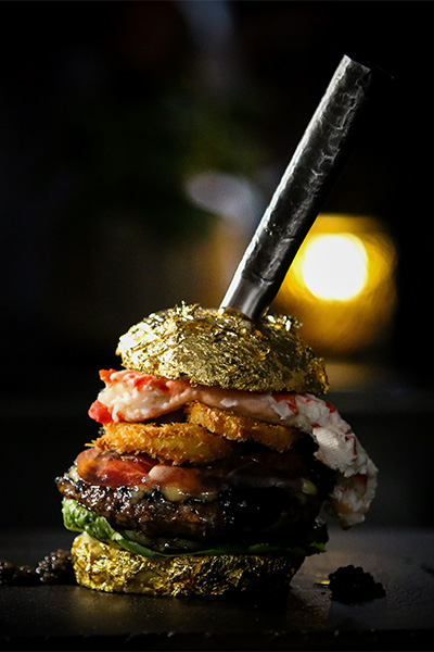 a burger with gold on top and a knife sticking in it