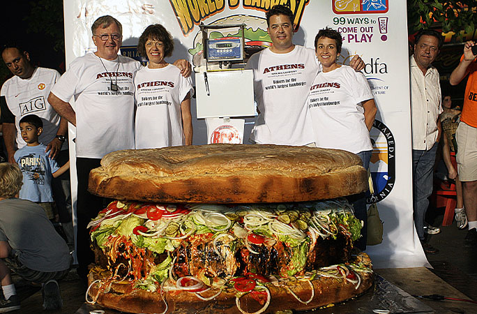 a giant burger with a group of people standing behind it