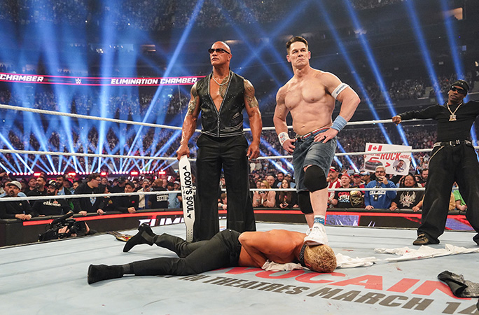 Dwayne The Rock Johnson in the ring with John Cena who has one foot on Cody Rhodes head