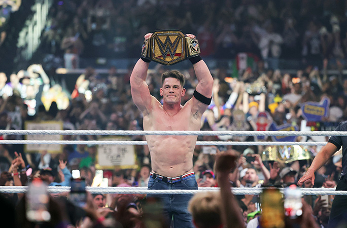John Cena in the ring holding his WWE championship belt being cheered on by the crowd