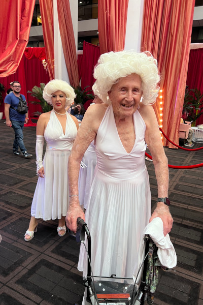 Older man dressed as Marilyn holding a walker indoors
