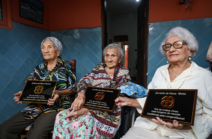 The three sisters sitting holding plaques from LongeviQuest