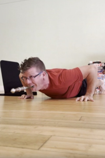 Close up of Noah doing a push up with a sword in his mouth