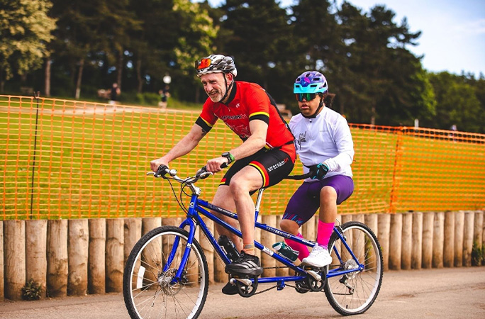 Michael cycling on a tandem bike with another man