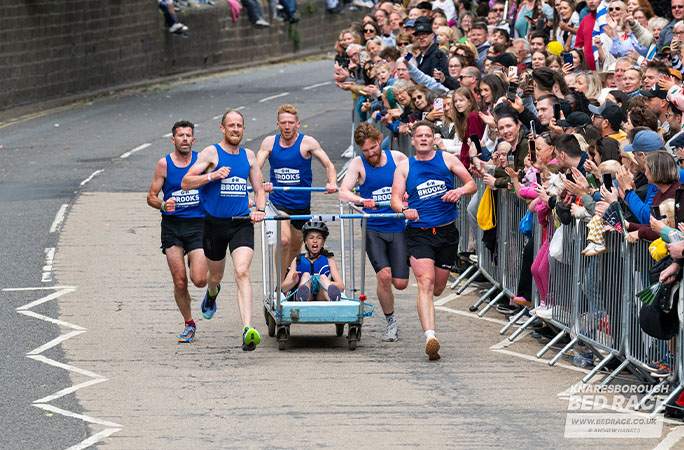 bed race team running past a crowd
