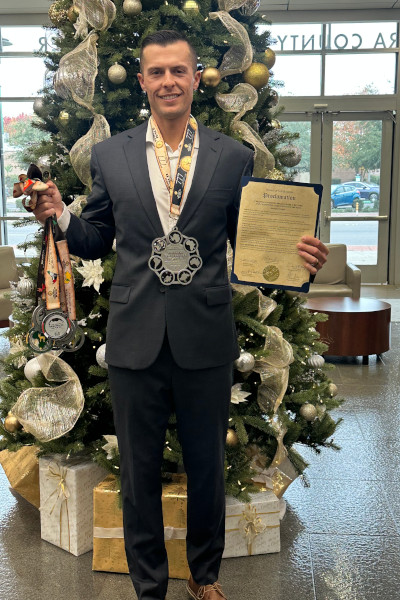 Christian showing off his medals next to a Christmas tree