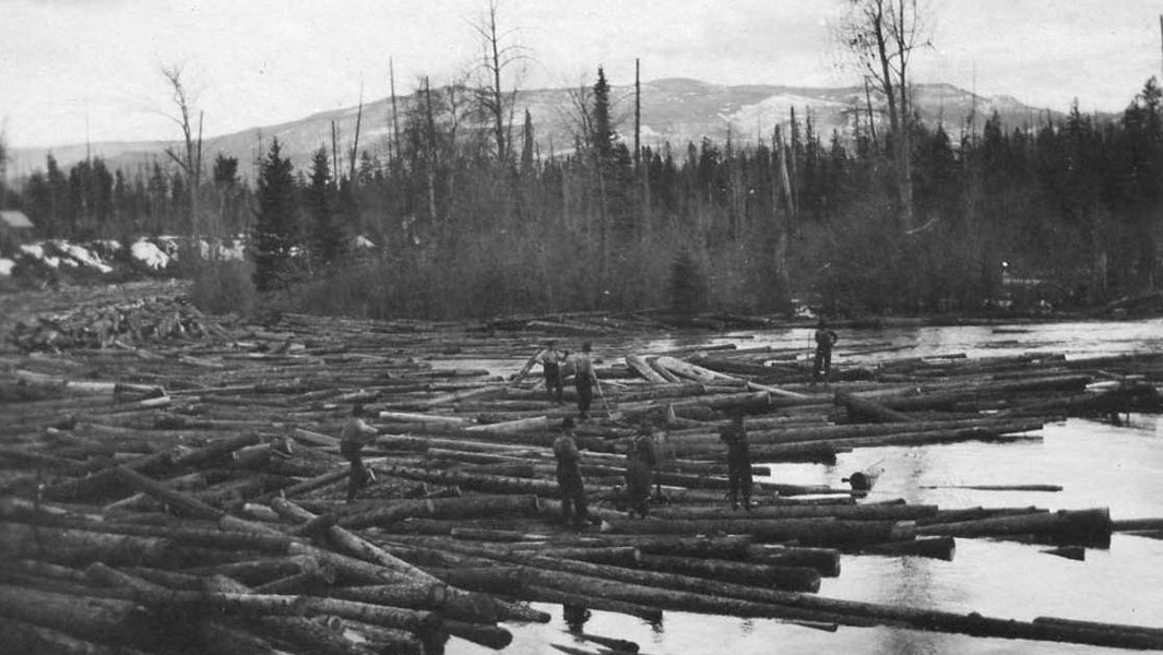 A black a white photo of workers moving logs on a river in Montana