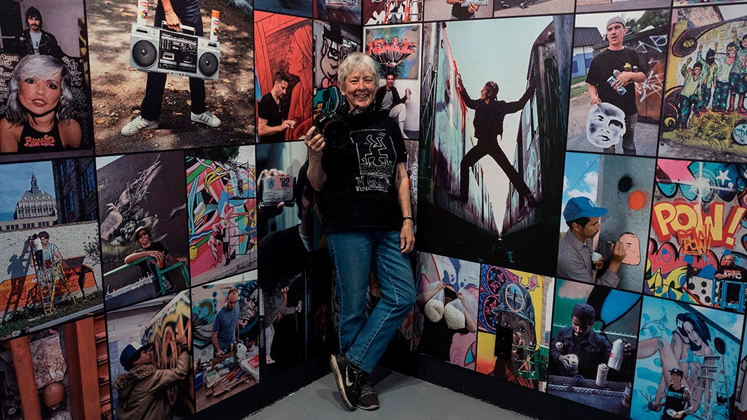martha-cooper-with-camera-and-at-one-of-her-exhibitions