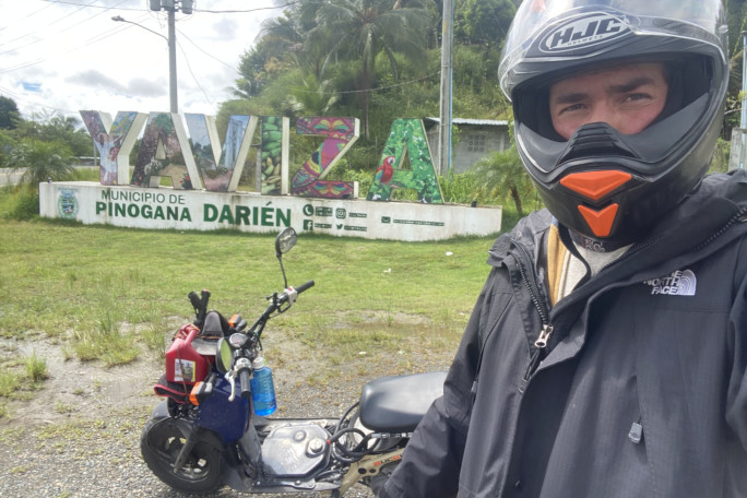 Jon taking a selfie with his moped at the Darien Gap sign