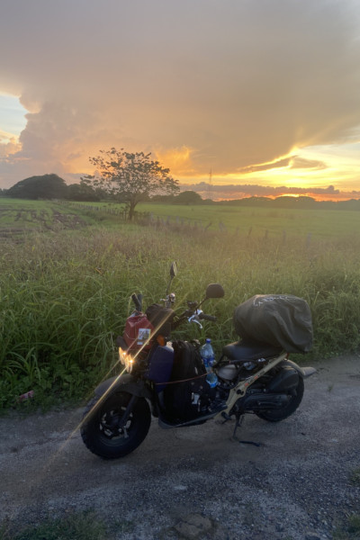 A photo of the moped under a sunrise in a scenic field