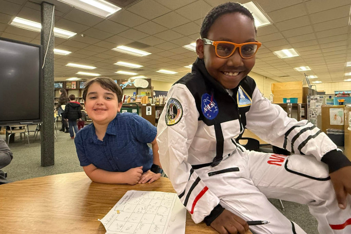 Skyler in a NASA suit sitting next to his friend